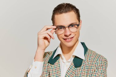 Entelektüel. Eski moda ceketli yakışıklı bir adamın portresi gri arka planda büyüleyici bir gülümsemeyle kameraya bakıyor. Eski moda kavramı, tarz, olumlu duygular, reklam.