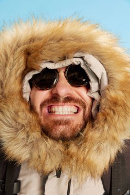 Kocaman gülümse. Güneş gözlüklü sakallı adamın yakın plan portresi mavi arka planda canlı duygular ifade ediyor. Retro stil kavramı, duygular, yüz ifadesi, spor. Kış modası