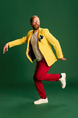 Hippi. Yeşil arka planda izole edilmiş parlak ceketli ve pantolonlu şık olgun bir adamın portresi. Tarz kavramı, yaratıcılık, duygular, yüz ifadesi, moda, meslek