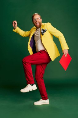Hippi. Yeşil arka planda izole edilmiş parlak ceketli ve pantolonlu şık olgun bir adamın portresi. Tarz kavramı, yaratıcılık, duygular, yüz ifadesi, moda, meslek