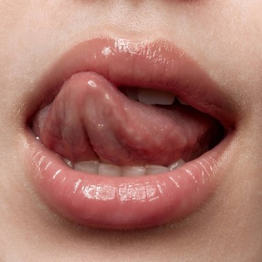 Dudaklarını yalıyor. Çıplak ruj sürmüş seksi kadın dudakları. Şehvetli kadınlar ağızlarını dilleriyle açarlar. Güzellik, moda, tarz konsepti, kırpılmış görüntü