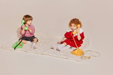 İki sevimli çocuk, kız kardeş ve erkek kardeş yerde oturup gri arka planda izole bir şekilde oyun oynuyorlar. Mutlu çocukluk kavramı, boş zaman aktiviteleri, eğlence, yaşam tarzı, aile, eski tarz