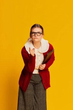 Sarı arka planda poz veren eski moda kıyafetler giyen genç bir kız. Eski moda, iş, eğitim ve duygular. İlan için alanı kopyala