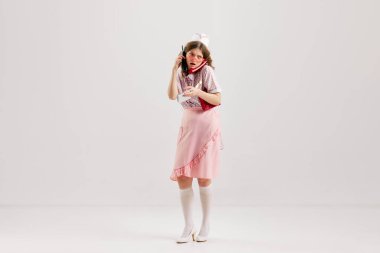 Emotional young woman, retro waitress in american fashion style of 70s, 80s uniform posing over light studio background. Comic photography style. Concept of emotions, job occupation, ad, cafe service