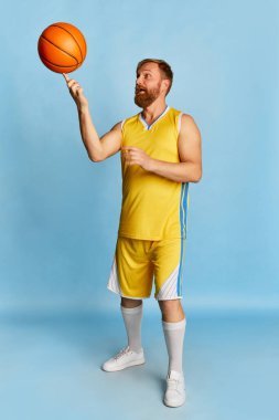 Active happy man with beard wearing sportswear playing basketball isolated over blue background. Concept of active lifestyle, positive emotions, sport, fitness, ad