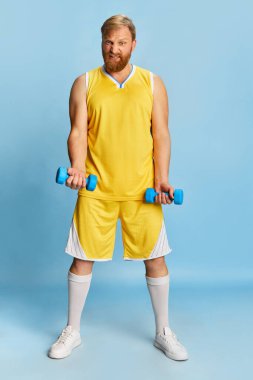 Active happy man with beard wearing sportswear doing exercises, workout isolated over blue background. Concept of active lifestyle, positive emotions, sport, fitness, ad