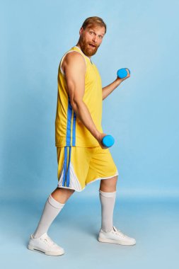 Active happy man with beard wearing sportswear doing exercises with weights, workout isolated over blue background. Concept of active lifestyle, positive emotions, sport, fitness, ad