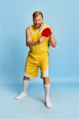Excited happy man with beard wearing sportswear playing ping-pong isolated over blue background. Concept of active lifestyle, positive emotions, sport, fitness, ad