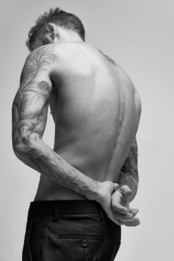 Black and white portrait of handsome young man posing shirtless. Textured body shape. Male accessories. Body art. Concept of fashion, style, body aesthetics, beauty, mens health