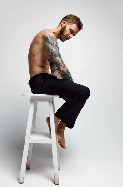 Stylish handsome young man posing shirtless. Textured muscular body shape. Tattoo body art. Concept of fashion, style, body aesthetics, beauty, mens health. Model loooks calm and composed