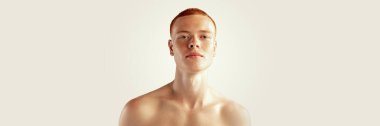 Handsome young red-haired man posing isolated over grey studio background. Male natural beauty. Concept of mens health, posing, beauty, body and skin care. Horizontal banner
