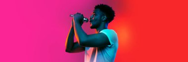 Singer. Horizontal banner with portrait of young african man over background in neon light. Beauty, fashion, youth and music concept. Copy space for ad, text
