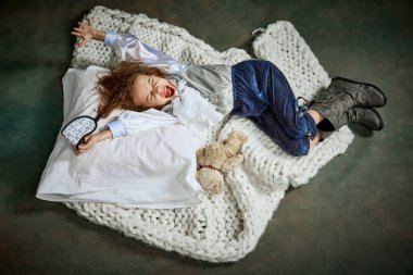 Happy morning, excited wake up. Ariel view of cute little girl in clothes sleeping on white blanket. Concept of napping day, dreams, happy childhood. Kid shouting with joy