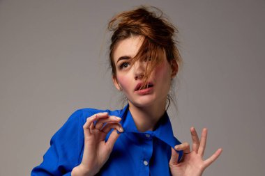 Fashionable stylish emotional woman wearing blue shirt posing over gray background. Model with vivid facial expression. Concept of fashion, style, youth, beauty. Closeup