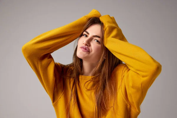 Half-length portrait of fashionable sensual emotional woman wearing trendy yellow sweater posing over gray background. Concept of fashion, style, youth, beauty. Diversity of emotions