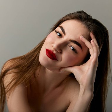 Closeup portrait of beautiful brunette model girl with long straight hair and bright red lipstick on lips. Concept of beauty, fashion, style, emotions. Model with well-kept skin and bare shoulders