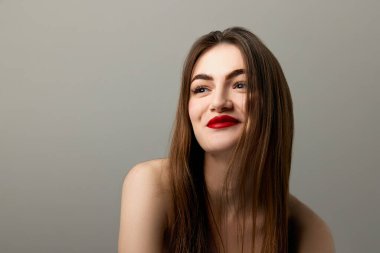 Closeup portrait of beautiful brunette model girl with long straight hair and bright red lipstick on lips. Concept of beauty, fashion, style, emotions. Model with well-kept skin and bare shoulders