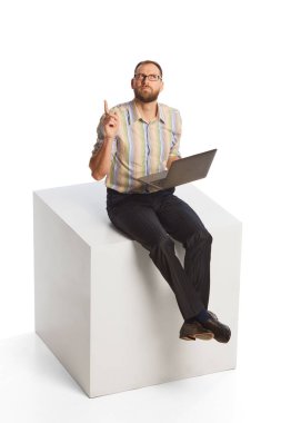 Young thoughtful business man dressed in casual office style clothes sitting and using laptop isolated on white background. Business, work, career, education concept.