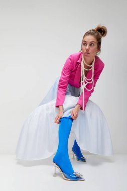 Runway fashion, style and image. Young expressive woman in blue tights and white skirt in motiona and action isolated over light background. Concept of high fashion, beauty, ad. Looks stylish