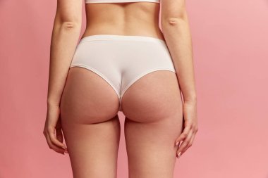 Back view of cropped female body in white inner wear isolated over pink background. Anti-cellulite care cosmetology. Concept of beauty, body care, health, plastic surgery, fashion, cosmetics, spa, ad