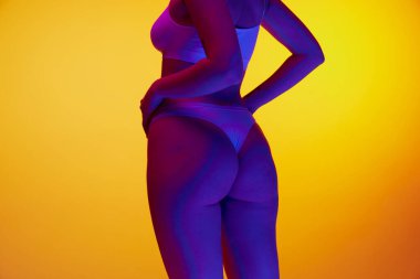 Silhouette of beautiful slim woman wearing underwear lingerie posing over orange studio background in purple neon light. Concept of beauty, body and skin care, health, plastic surgery, cosmetics