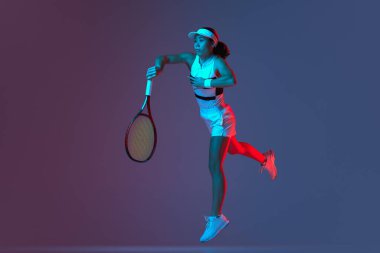 Studio shot of active professional tennis player training with tennis racket over gradient pink-purple background in neon light. Concept of sport, health, strength, action, motion, lifestyle.