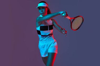 Portrait of young professional emotional tennis player in sports uniform in motion, action over gradient pink-purple background in neon light. Sport, fashion, energy, motivation concept