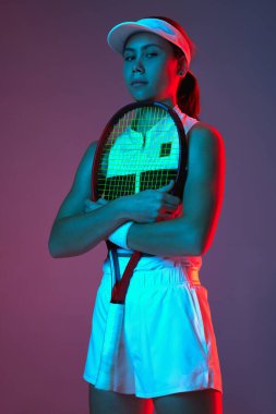 Young sportive girl professional tennis player posing with tennis racket gradient pink-purple background in neon. Concept of sport, strength, professional skills, active lifestyle and beauty, ad.