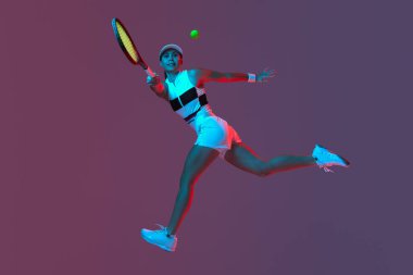 Studio shot of active professional tennis player training with tennis racket over gradient pink-purple background in neon light. Concept of sport, health, strength, action, motion, lifestyle.