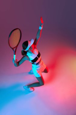 Aerial view of active professional tennis player serving over gradient pink-purple background in neon light. Concept of sport, health, strength, action, motion, lifestyle.