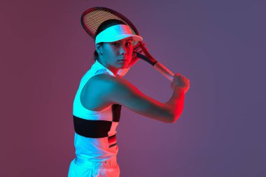 Young sportive girl professional tennis player posing with tennis racket gradient pink-purple background in neon. Concept of sport, strength, professional skills, active lifestyle and beauty, ad.