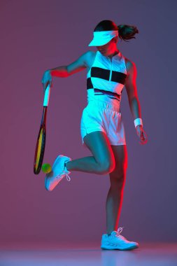 Studio shot of active professional tennis player training with tennis racket over gradient pink-purple background in neon light. Concept of sport, health, strength, action, motion, lifestyle.