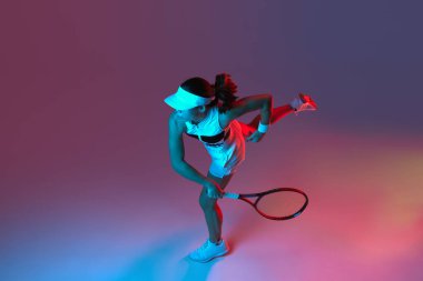 Aerial view of active professional tennis player training with tennis racket over gradient pink-purple background in neon light. Concept of sport, health, strength, action, motion, lifestyle.