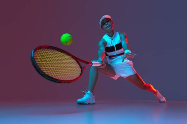 Wide angle view of active professional tennis player training with tennis racket over gradient pink-purple background in neon light. Concept of sport, health, strength, action, motion, lifestyle.