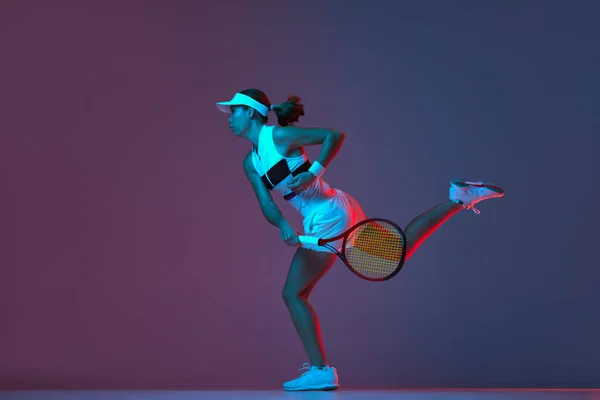 Portrait of young professional emotional tennis player in sports uniform in motion, action over gradient pink-purple background in neon light. Sport, fashion, energy, motivation concept