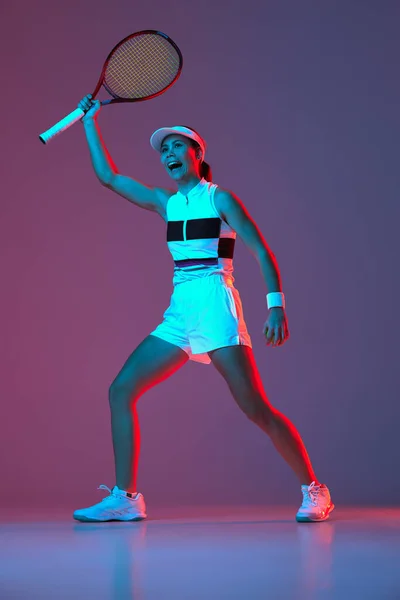 Winner. Portrait of young professional emotional tennis player in sports uniform in motion, action over gradient pink-purple background in neon light. Sport, energy, motivation concept