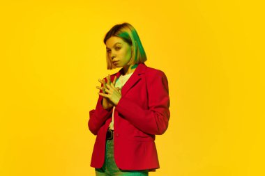 Sarı saçlı, kırmızı ceketli, sarı arka planda poz veren çekici bir genç kız. Gençlik kavramı, üniversite hayatı, iş ve eğitim. Model düşünceli görünüyor.