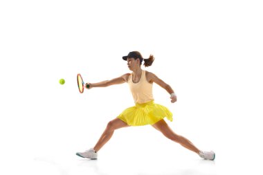 Studio shot of professional young female tennis player in sports uniform training with tennis racket isoltaed over white background. Concept of sport, health, strength, action, motion, lifestyle.