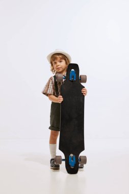 Skateboarder. Studio shot of little boy, preschool age kid wearing retro style clothes isolated over white background. Concept of emotions, 60s vintage fashion style, childhood, leisure activities