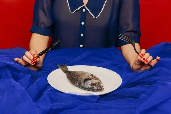 Food pop art photography. Cropped image of young girl cutting raw fish with knife over red background. Weird taste. Vintage, retro style. Concept of beauty, creativity, fashion, ad