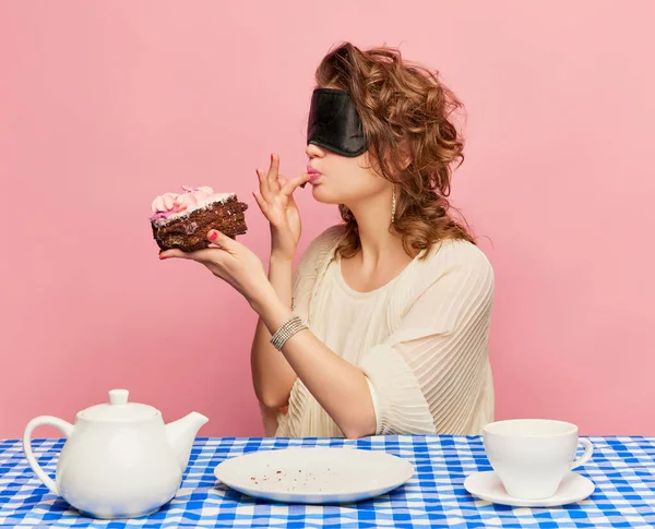 Young girl with tousled hair after sleep and with sleep mask eating cake, pie and drinking tea. Concept of emotions, weird people, retro fashion and humor. Food pop art photography