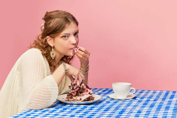 Delicious taste. Charming young girl eating cake, pie and drinking tea. Sweet cream mask. Concept of emotions, weird people, retro fashion and humor. Food pop art photography
