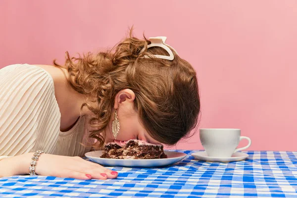 After birthday party. Young girl with tousled hair after night sleeping at cake, pie over pink background. Concept of emotions, weird people, retro fashion and humor. Food pop art photography