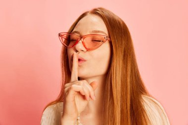 Keep secrets. Closeup young beautiful redhaired girl with long hair isolated over light pink background. Concept of positive emotions, happy mood, beauty, fashion and active youth lifestyle