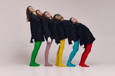 Art, beauty. Studio shot of young stylish beautiful fashion models in black jackets and multi colored tights posing over grey background. Concept of feminism, extraordinary fashion, modern style