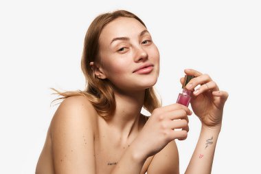 Happy young beautiful girl with long blonde hair holding moisturizing lotion, serum for face skin. Model with bare shoulders. Concept of skin care, beauty, spa, anti-aging procedures