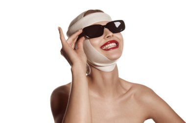 Lifting, therapy. Female face bandaged with medical bandages and sunglasses with human emotions. Making beauty, modifying face to make surgical correction, plastic surgery. correction of asymmetry.
