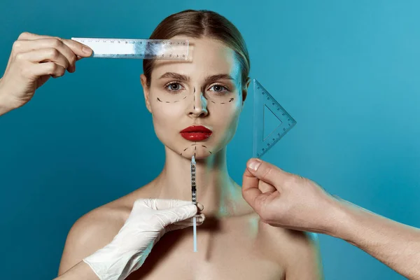 Plastic surgery or face lifting for young woman. Doctors hands wearing gloves drawing lines, holding head of female patient. Making beauty, modifying face to make surgical or non-surgical correction