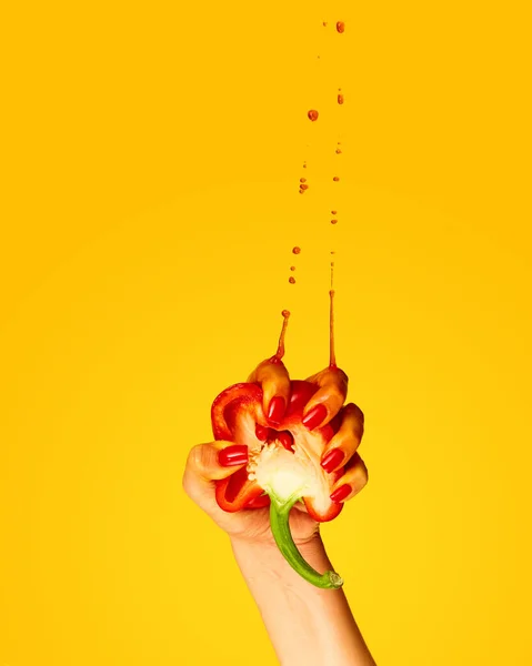 Red pepper juice. Female hand squeeze pepper and drops flying up over yellow background. Pop art, surrealism, gravity and taste concept. Copy space for ad