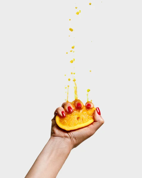 Fresh juice. Female hand with bright manicure squeezes half of orange. Pop art food photography. Drops of juice fly up. Concept of healthy eating, art, fashion, creativity and ad